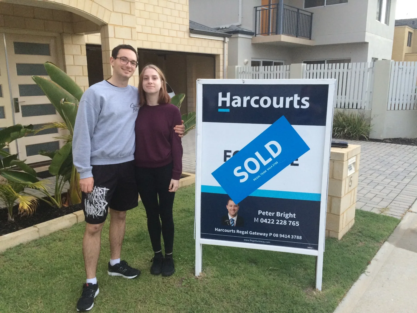 Aaron and Cheyenne beside the sold sign at their first property